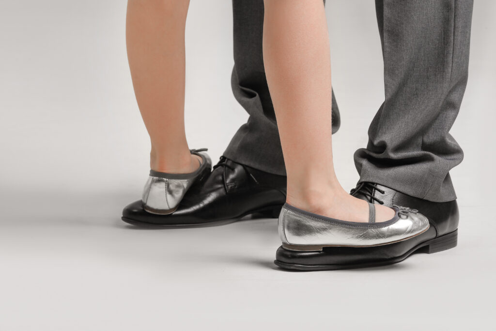 Legs of father and his little daughter dancing against grey background